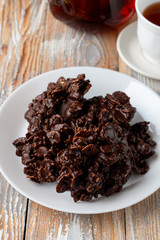 Close up of corn flakes cookies, coated in dark chocolate, with a cup of black tea on old wooden table
