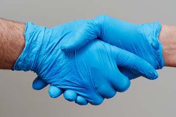 two people shaking hands wearing surgical gloves
