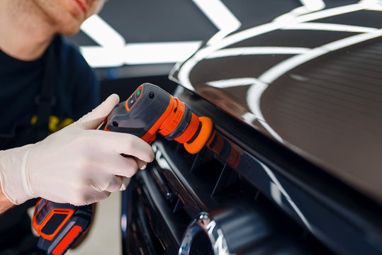 Worker polishes radiator grille, car detailing