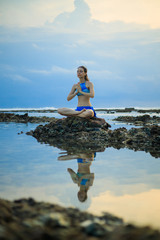 Young woman, meditating, practicing yoga and pranayama at the beach. Sunset yoga practice. Hands in...