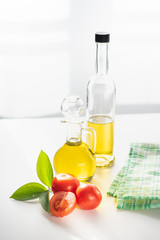 on a white background vegetable olive oil in a glass decanter. Nearby are slices of tomatoes and a green leaf.