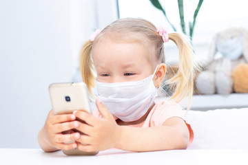 girl in a protective medical mask using a mobile phone, a smartphone for video calls, talks with relatives, a girl sits at home, online computer webcam, making a video call.