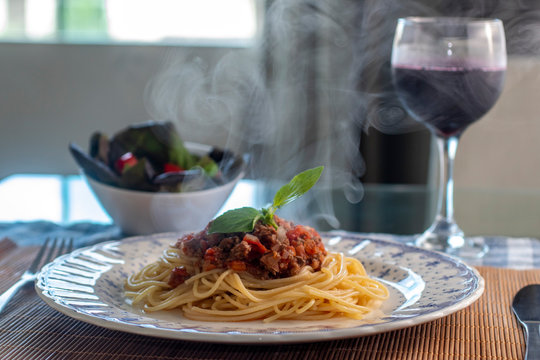 spaghetti pasta with bolognese sauce with steam and smoke and glass of wine