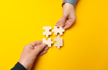 Two hands connect puzzles on a yellow background. Cooperation and teamwork in business....
