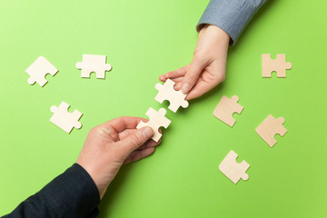 Two hands connect puzzles on a green background. Cooperation and teamwork in business....
