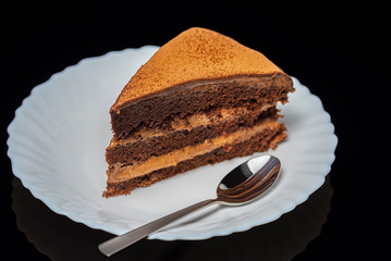 Piece of cake Theremis on a white plate on a dark background. Photographed close-up.
