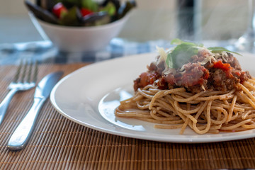 
wholemeal spaghetti pasta with bolognese sauce and basil on a white plate