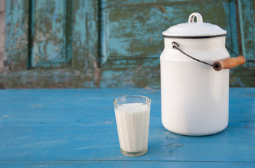 glass glass of milk and an old metal can with a lid and a handle stand on a blue background