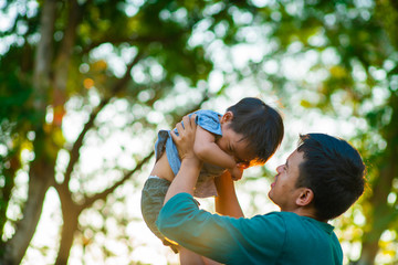 Portrait of happy father holding baby son hand carry up in city park sunset light.