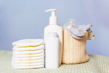 Newborn baby care products. Lotion, powder and diapers on changing table in nursery. Baby's nipple and socks in knitted basket. Baby cosmetics and hygiene concept.