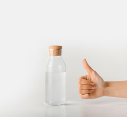Hand with thumb up next to a glass bottle with clear water.