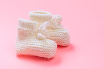 knitted baby booties on pastel pink background.