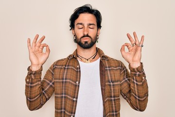 Young handsome hispanic bohemian man wearing hippie style standing over isolated background relax and smiling with eyes closed doing meditation gesture with fingers. Yoga concept.