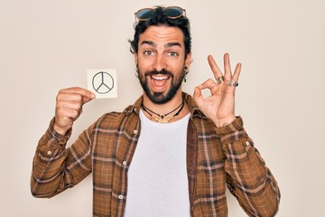 Fototapeta premium Young handsome hispanic bohemian hipster man with bear holding paper note with peace symbol doing ok sign with fingers, excellent symbol