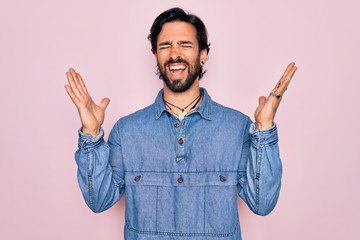 Young handsome hispanic bohemian man wearing hippie style over pink background celebrating mad and crazy for success with arms raised and closed eyes screaming excited. Winner concept