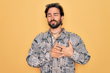 Young handsome hispanic bohemian man wearing hippie style and sunglasses smiling with hands on chest with closed eyes and grateful gesture on face. Health concept.