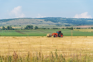 Tractor lifting hay bale on barrow.
