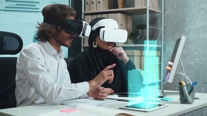 international business meeting, man and muslim woman in virtual reality glasses exploring the futuristic hologram layout of a business center, demonstration of the architecture using augmented reality