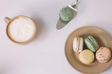 Homemade colorful macarons on the brown plate on the white background. Cup of coffee. Blossom.