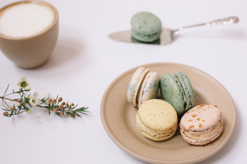Homemade colorful macarons on the brown plate on the white background. Cup of coffee. Blossom.