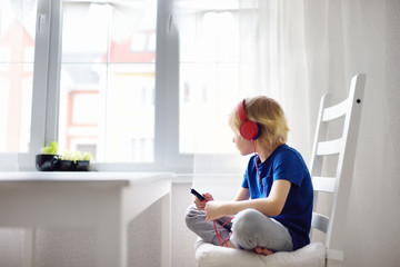 Preschooler child enjoy listen music or audiobook using his headphones at home.