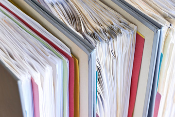 Closeup of binders with papers and tabs. Stack of business papers, bills or documents in standing document binders. Debt free life, business office stress workload or paperless office concept.   