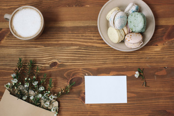 Colorful homemade macarons are lying on the brown wooden background.Cup of coffee. Envelope with blossom. Card with place for text.