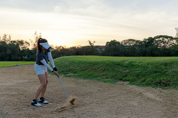 Asian Golfer woman hitting golf ball out of a sand trap. People with the golf course is on the sand.  Hobby in holiday and vacations on club golf. Lifestyle and Sport Concept.