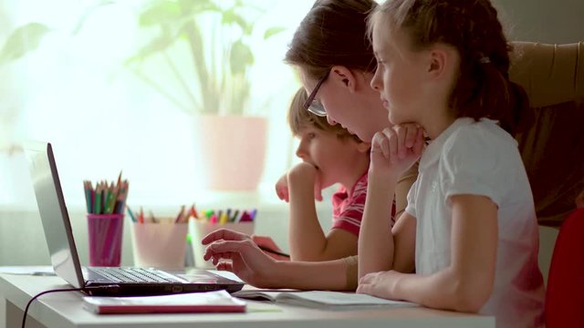 Cute children use laptop for education, online study, home studying, Boy and Girl have homework at distance learning. Lifestyle concept for Family quarantine covid-19. Mother helps daughter and son.