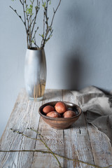  eggs lie in a cup and willow branches lie on a wooden table and a gray background. Rustic 