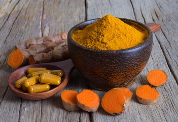 Turmeric powder in a black wooden bowl, capsules in a wooden ladle and fresh turmeric (curcumin) on wooden background.