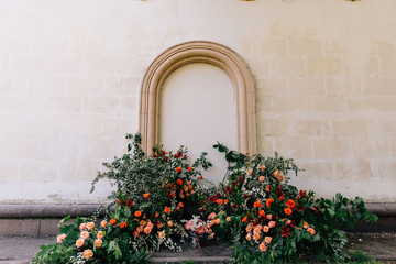 the unusual area of the wedding venue on the background of the wall with stucco is decorated with fresh flowers in the form of thickets and the main color accent coral