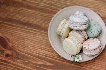 Colorful homemade macarons are lying on the beige plate on the brown wooden background. Pattern.
