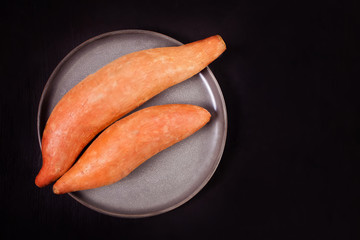 Raw sweet potatoes on the black background. Top view.