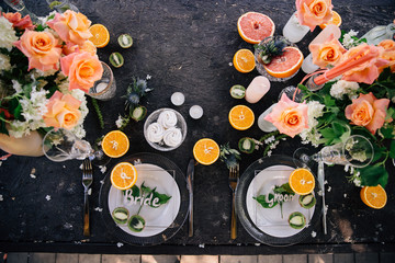 Plates for seating the bride and groom in a trend of glass on a dark wedding table with citrus fruit decorations