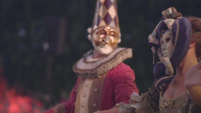 Two artists in venetian masquerade carnival masks and vintage costumes dance against the backdrop of a green forest on a summer evening