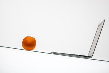 laptop on a glass table with an orange on a white background