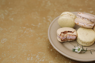 Yellow homemade macarons with blossom are lying on the brown plate on the golden background.