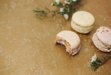 Three homemade macarons with blossom are lying on the golden background.