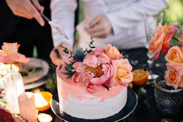 bride and groom cut a wedding cake decorated with fresh flowers in coral color
