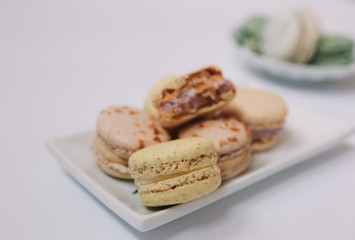 Home made macarons are lying on the white plate on white background with green and white macarons in plate