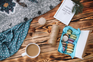 Homemade colorful macaroons in the box are lying on the brown wooden table with cup of coffee and...