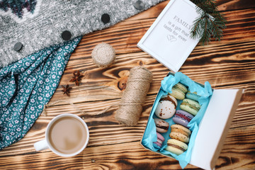 Fototapeta na wymiar Homemade colorful macaroons in the box are lying on the brown wooden table with cup of coffee and picture Family is a gift that lasts forever. Cup of coffee. Anise, honey and colorful tissue.