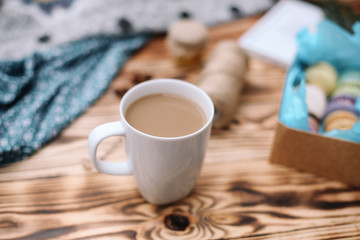 Two homemade colorful macaroons are lying on the brown wooden table with cup of coffee. Cup of coffee. Colorful tissue.