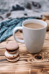 Two homemade colorful macaroons are lying on the brown wooden table with cup of coffee. Cup of coffee. Colorful tissue.