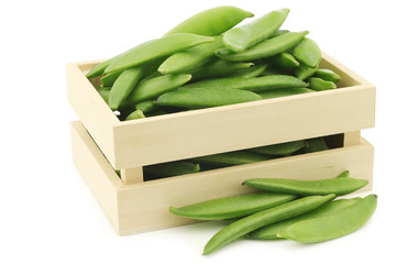 freshly harvested sugar snaps in a wooden box on a white background