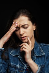 Unhappy young woman touching her heads and suffering from headache. Dark background. People, emotions, stress and health care concept.