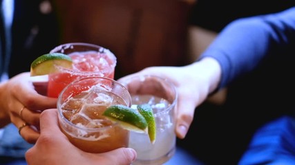 Friends toasting, saying cheers holding tropical blended fruit margaritas. Watermelon, tamarind, and lime drinks and cocktails.
