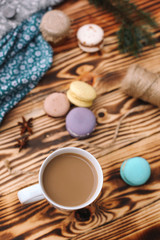 Homemade colorful macaroons are lying on the brown wooden table with cup of coffee. Cup of coffee. Anise, honey and colorful tissue.