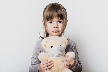 Uen petite fille tenant son ours en peluche avec un masque pendant la période du confinement du...